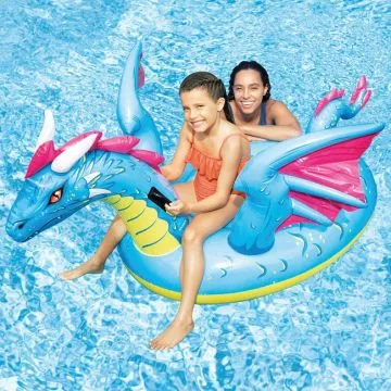 A girl and a woman smile while sitting on a large blue and pink inflatable dragon pool float in a swimming pool.