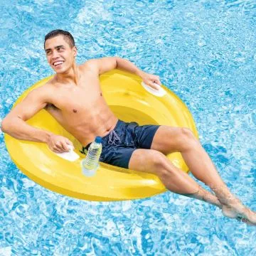 A smiling man wearing blue swim trunks relaxes on a bright yellow inflatable pool float, holding a plastic water bottle, in a swimming pool.