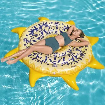 
A person relaxing on a large, yellow and blue sun-shaped pool float in a swimming pool. The float has a Mediterranean-inspired pattern.
