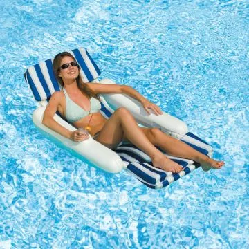  A woman in a light blue bikini and sunglasses sits on a white, rigid pontoon-style pool lounge chair with a blue and white striped padded seat and backrest in a swimming pool, holding a drink.