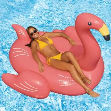 Person lounging on the pink flamingo pool float in a sunny backyard pool setting