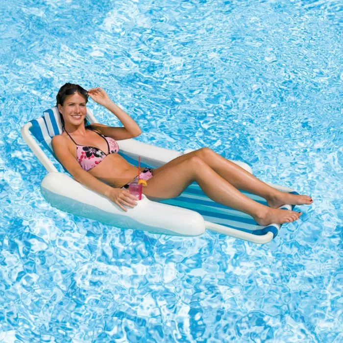 Swimline Sunchaser Sling - A smiling woman in a pink floral bikini relaxes on a white and blue striped inflatable pool lounge chair in a swimming pool, holding a drink. Swimline Sunchaser Sling - A smiling woman in a pink floral bikini relaxes on a white and blue striped inflatable pool lounge chair in a swimming pool, holding a drink.